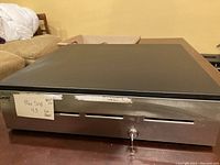 Top and front view of the large cash drawer showing black top and stainless steel front with slots and lock
