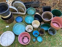 Overview of assorted planters and saucers on the ground showing multiple colors and sizes, some dirt visible