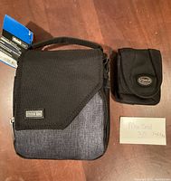 Photo of two camera bags on wooden surface, one larger Think Tank bag with tag and a smaller black Tamrac pouch with flap closed