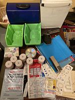 Photo showing a variety of office supplies including receipt paper rolls, DVD-R discs, green plastic bins, folders, stencils, and a small paper shredder.