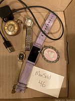 Top-down overview of the pocket watch, Fitbit with charger, two wristwatches and cameo brooch.