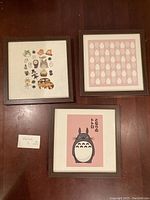 Three framed Studio Ghibli Totoro prints laid out showing different character designs and prints on brown wooden frames.