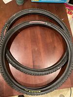 Two Maxxis Ignitor 26 x 2.1 black mountain bike tires placed on a wooden surface, showing full view of tread and sidewalls with clear branding and model.