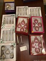 Lot of vintage Christmas ornaments in original and unopened Alderrrock boxes, assorted shapes including teardrop and spherical in silver, white, and pink tones, as well as some loose ornaments.