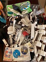 Photo showing a large assortment of Wii accessories including various sports attachments, controllers, charging dock, and multiple game discs in white trays.