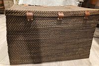 Front view of the woven basket chest showing leather strap detailing and textured weave pattern.