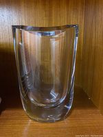 Clear thick glass vase with curved sides, shown on wooden shelf for scale.