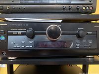 Front view of Panasonic SA-HE9 AV control receiver showing control knobs, buttons, and display.