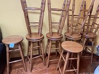 10 oak bar height barstools shown in a row against a wall, displaying their backs and seats.