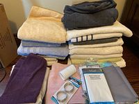 Stack of assorted bath and hand towels in various colors with shower curtain packages, hooks and rings laid out