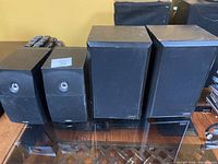 Four black bookshelf speakers of Szabo Audio brand, two smaller pairs with fabric covers and two larger pairs behind, showing fabric wear and some cabinet scratches.