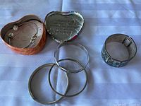 Lot displayed on white cloth, showing three simple sterling silver bangles, one abalone inlaid sterling silver wide bangle, and a wide bangle with blue abalone shell inlay with burnished silver edges.