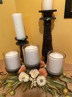 Full view of both dark wood pillar candle holders with white candles, together with the fall-themed centerpiece with three glass containers holding candles decorated with small white pumpkins, berries, and leaves.