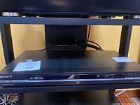 Front view of black Sony CD/DVD player showing front tray and control buttons.