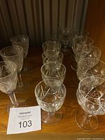 Collection of 14 crystal stemmed glasses of varying size and cut patterns placed on wooden surface.