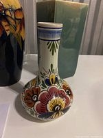 White Delft pottery vase with colorful floral hand-painted decorations, bulbous shape with narrow neck, displayed with other vases.
