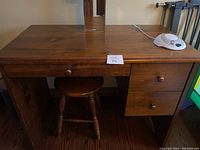 Full frontal photo of wooden desk with matching stool underneath, showing desk surface, drawer fronts, and stool legs.