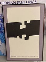 Front view of the abstract framed print by Eduardo Chillida showing black geometric shapes on cream background with text below.