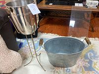 Silver metal ice bucket on gold-tone three-legged stand with wooden side handles, set on carpet with pattern.