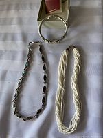 Photo of all three jewelry items on cloth background: multi-strand white glass bead necklace, abalone necklace, pewter bracelet with box