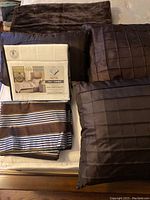 Bed linens, cushions, curtains, and throw blanket arranged on bed showing full contents of the lot.