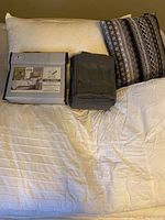 Bed with white fitted sheet, white pillow, patterned accent cushion, folded gray sheets, new bed sheet set in packaging labeled 500 thread count full/double size