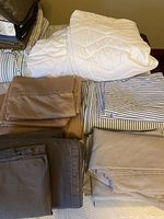 Photo showing the white quilted mattress protector folded with bedsheets in beige, brown, and blue-white stripes.