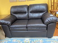 Front view of brown loveseat on rug and hardwood floor