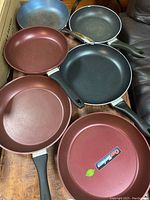 Six frying pans laid out showing different colors and handles, all non-stick