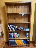 Full view of the solid pine Mennonite made bookcase filled with some books and other small items (to be excluded). Shows the entire front, shelves and natural wood finish.