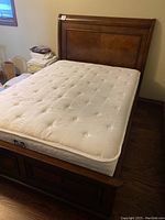 Full view of bed with mattress showing wooden platform sleigh bed with two drawers and cream tufted mattress