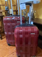 Two red Samsonite hard-shell suitcases with spinner wheels and extended telescoping handles standing upright on wooden floor against a yellow wall and furniture.