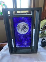 Full view of the Kosta Boda blue glass sculpture in wooden frame on table.