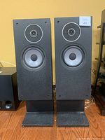 Front view of both black pedestal speakers showing tweeters and woofers