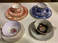 Four fine bone china teacups with matching saucers in red floral, blue scenic, and floral paint with gold trim styles.