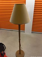 Full view of teak floor lamp with beige conical lampshade against an orange storage door background.