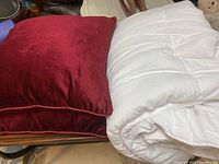 Two red decorative accent cushions alongside a rolled white lightweight comforter.