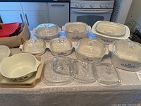 Wide shot of the complete set of bakeware on a table showing multiple ceramic dishes with blue floral patterns, clear glass lids, and a red carrying case.