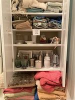 Full view of cabinet shelves with folded towels, soap dispensers, decorative jars, small mirror, and framed beach wall art.
