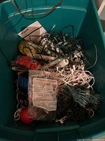 Clear view of assorted tangled Christmas lights, some with green and some with white wires, stored in a teal plastic bin along with various packaging and accessories.