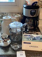Black and Decker coffee maker, glass French press, white ceramic carafe, Oneida cream and sugar set box on countertop