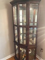 Full view of dark wood corner curio cabinet with glass shelving and door panels