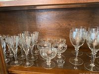 Full view showing assortment of various sizes of Bohemia crystal stemware with thistle pattern engraving on a wooden shelf