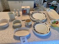 Photo shows a collection of Corelle square plates with black and white floral designs, multiple small bowls, salt and pepper set, and a boxed cream and sugar set arranged on a table.