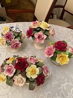 Four Aynsley floral porcelain arrangements including Queen's Floral, Royale, Stratford, and Crown patterns with mixed color flowers and leaves on various ceramic bases. One has visible hairline crack.