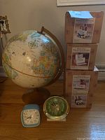 Photo showing vintage world globe with wooden stand, two vintage desk clocks, and three boxed new desk organizers stacked nearby.