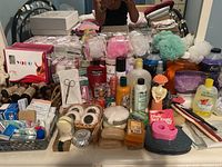 Full assortment of bath and personal care items displayed on bed including soaps, lotions, bath poufs, oils, and hair accessories