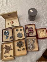Overview of eight brooch and earring sets displayed on table with fabric background