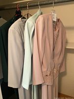Photo of four vintage ladies dresses hanging on a rack showing different colors and styles including pale pink, seafoam green, gray, and dark dresses.