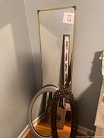 Three mirrors grouped together in corner, showing the tall rectangular brass framed mirror, white framed oval mirror, and ornate wooden oval mirror